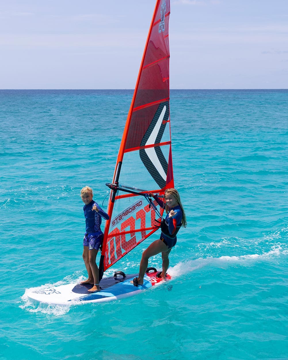 Two young windsurfers sharing a Starboard Go