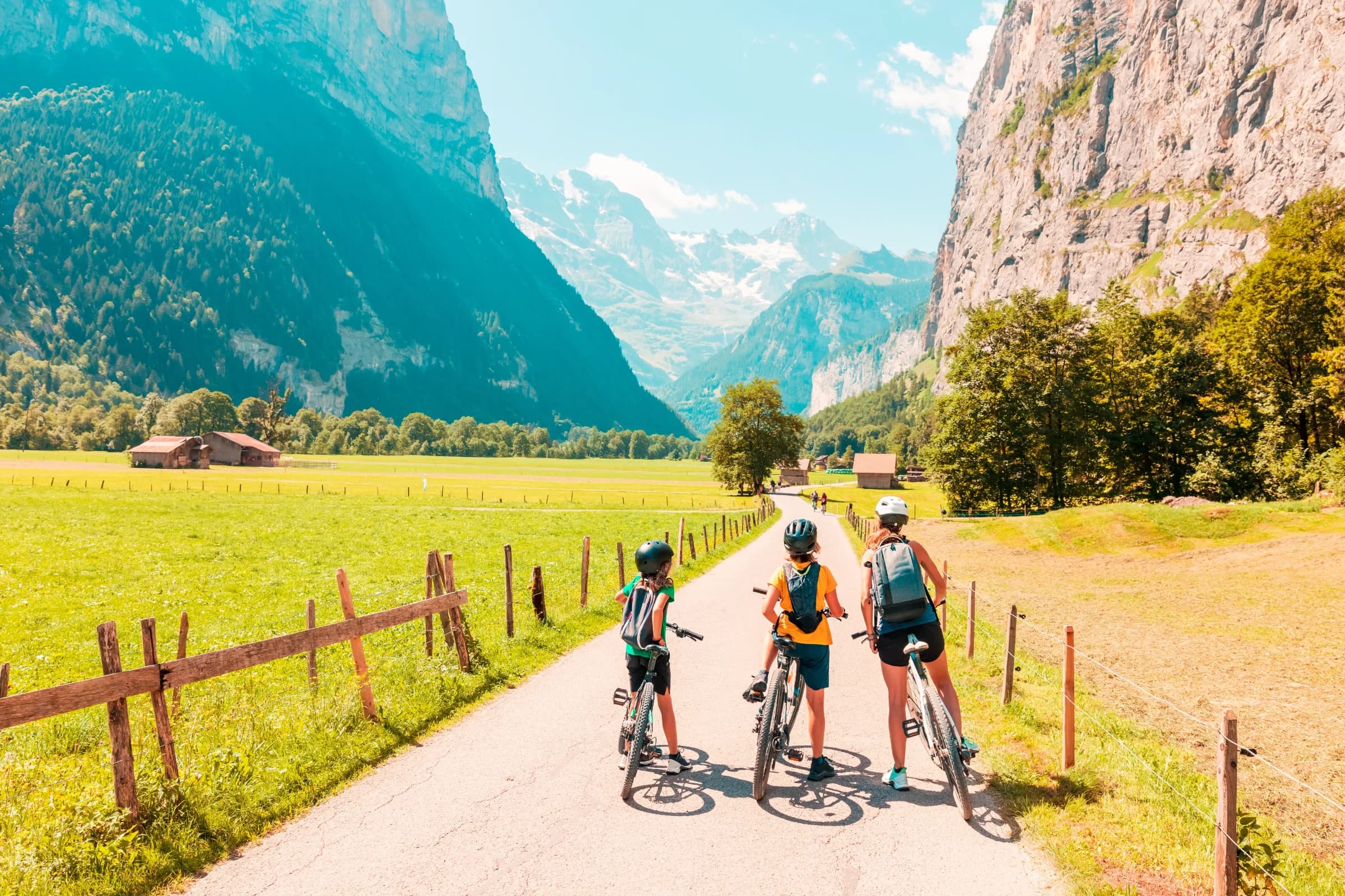 Three cyclists on a valley path with dramatic mountain cliffs and green meadows in Alpine scenery