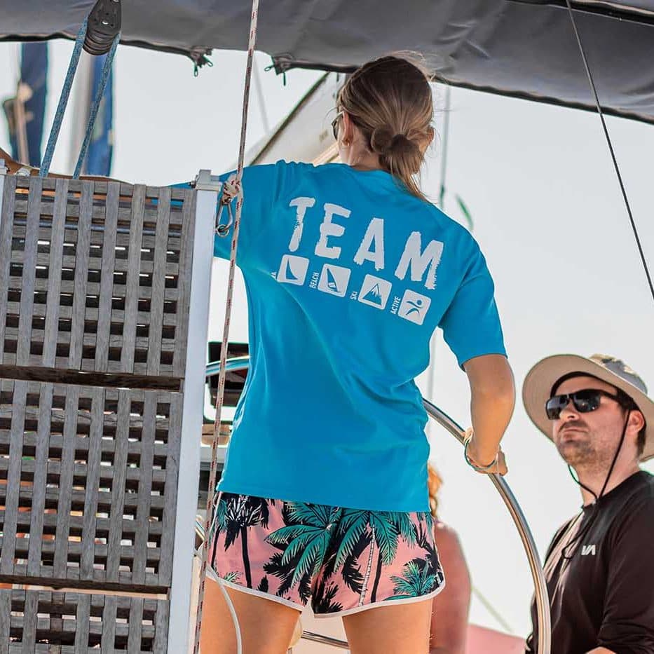 Crew member in blue team shirt on sailing boat with instructor nearby