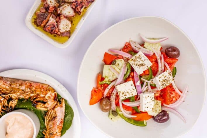 Greek salad with feta cheese, tomatoes, cucumbers, olives and red onions, alongside grilled fish and other local dishes from Kefalonia.