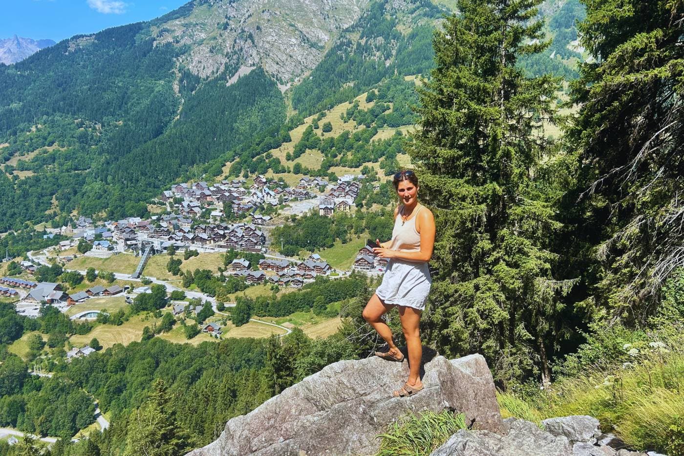 Runner on mountain outcrop overlooking Vaujany village nestled in forested Alpine valley, France