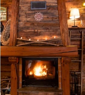 Open log fire burning under a rough-hewn timber mantel at Chalet La Grange d'Alice
