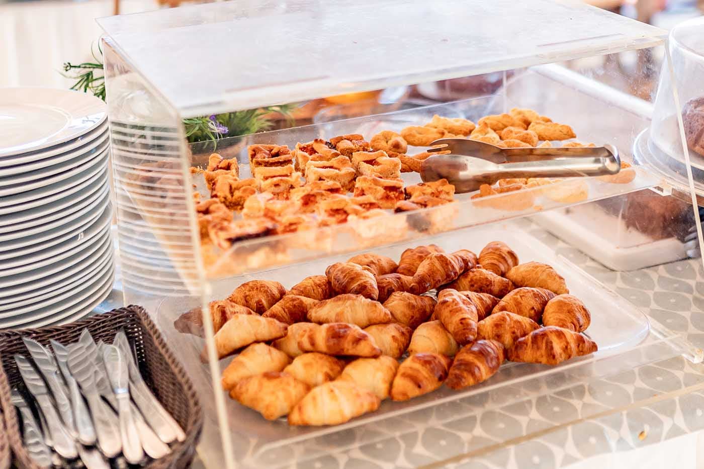 Pastries and croissants displayed at a Beach Clubs buffet in Kefalonia, Greece, with plates and utensils nearby